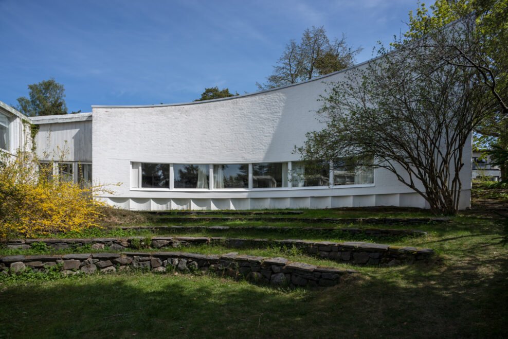 Fachada curva blanca y patio ajardinado de Studio Aalto en Helsinki.