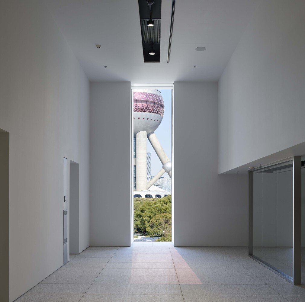 Interior blanco del Museum of Art Pudong de Jean Nouvel con una ventana enmarcando la Oriental Pearl Tower de Shangh&aacute;i