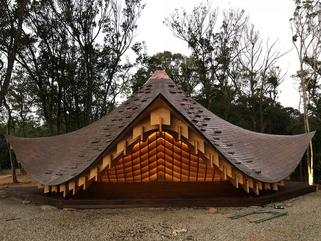 Pabellón de madera de Kengo Kuma con cubierta curva integrado en un entorno arbolado