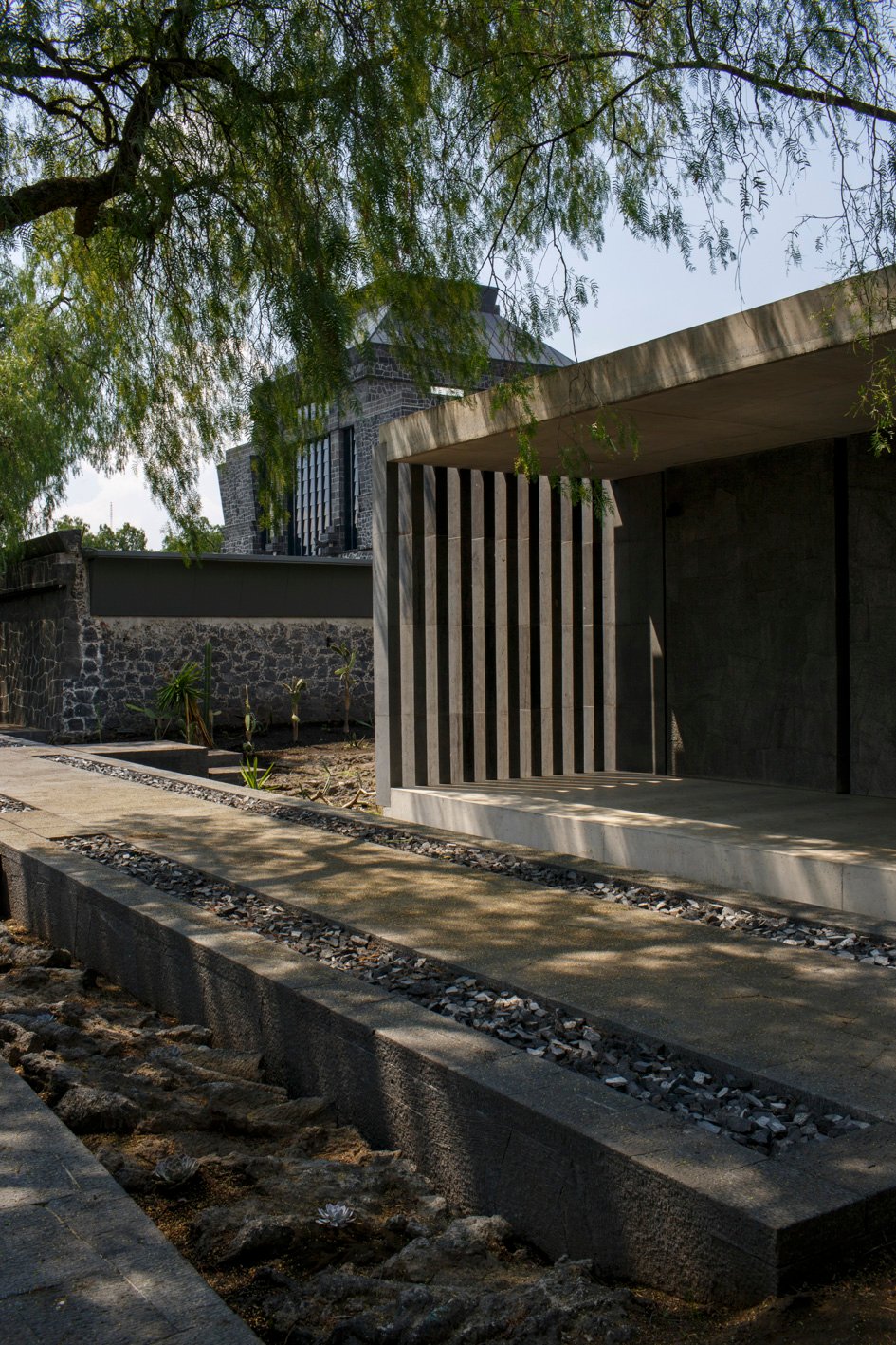 Biblioteca del Anahuacalli en primer plano y edificio original del museo al fondo, entre árboles y pasarelas.