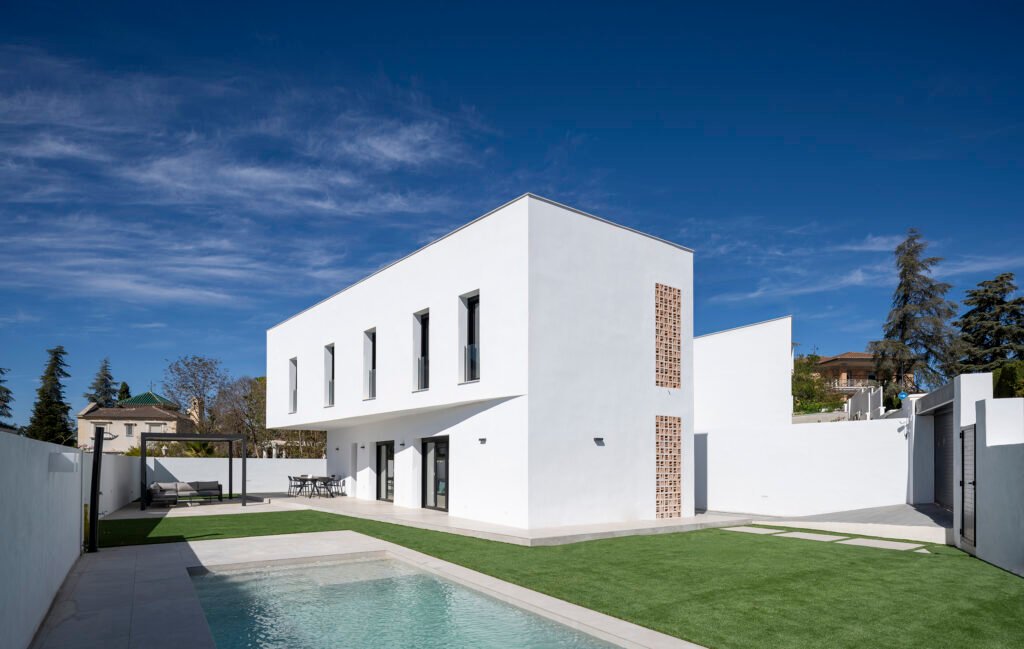 Vista de Casa Moreras con fachadas blancas, celosías verticales, porche y piscina en primer plano.
