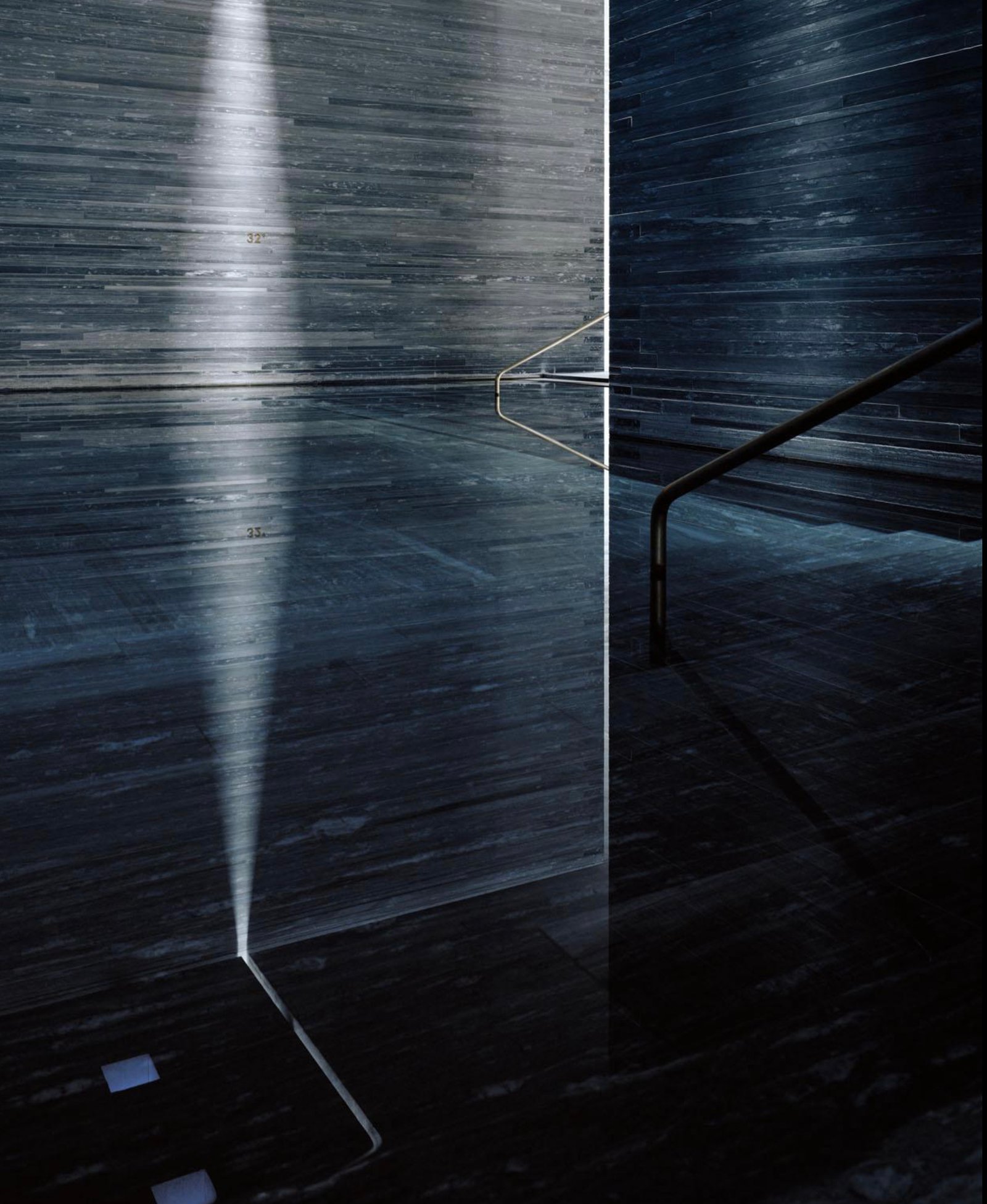 Interior de las termas de Vals, con paredes de piedra oscura, agua y una estrecha franja vertical de luz.