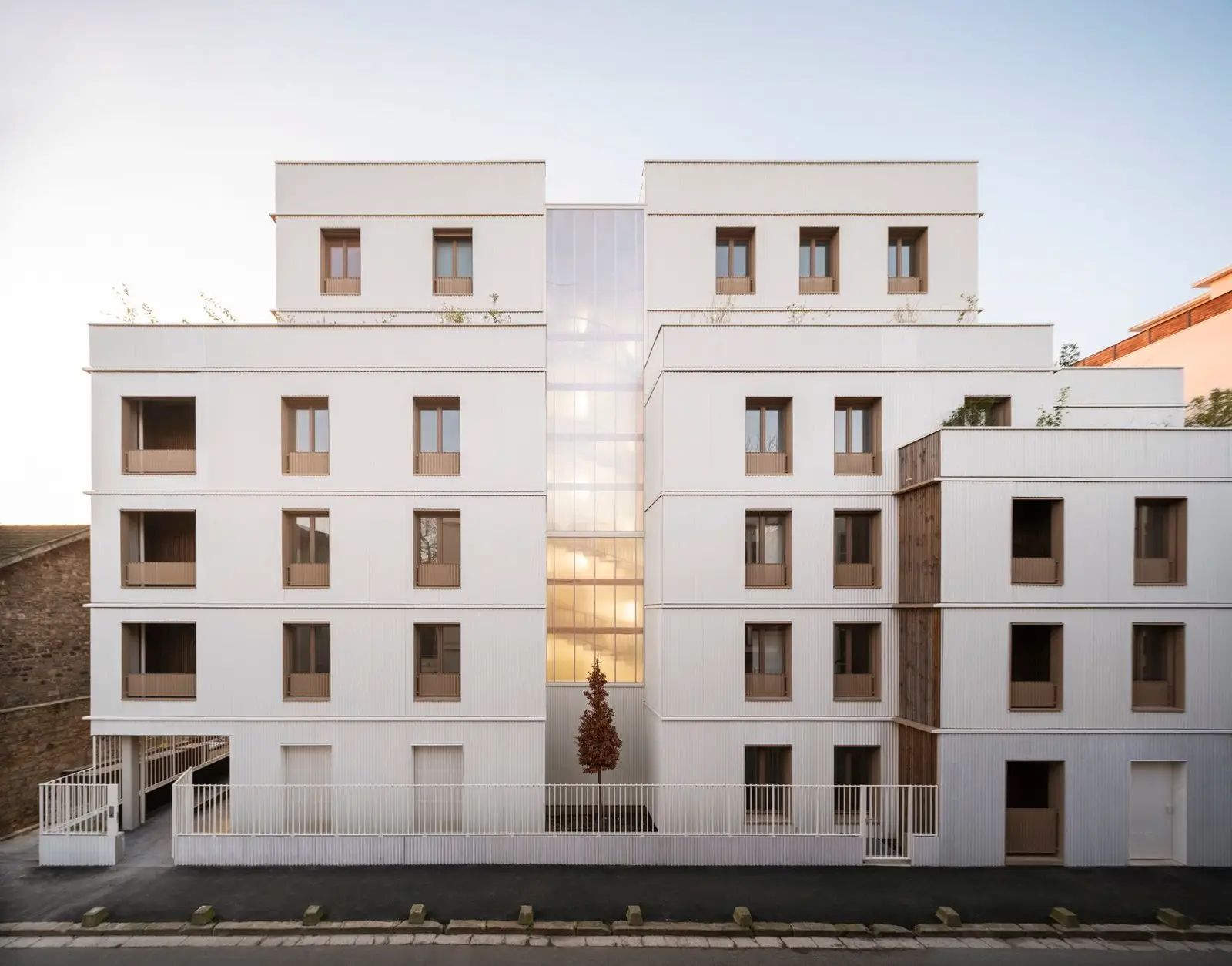 Fachada de 44 viviendas en Saint-Denis al atardecer, con núcleo translúcido iluminado