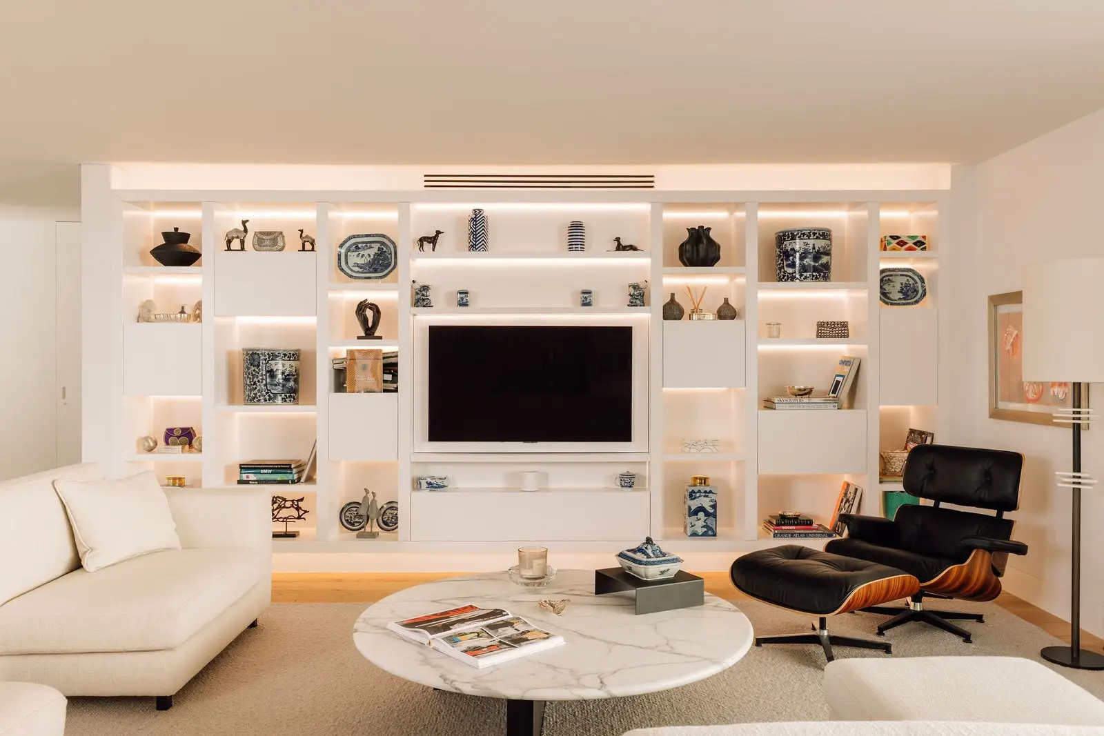Sal&oacute;n de Casa Restelo MVS con estanter&iacute;a blanca e iluminaci&oacute;n integrada