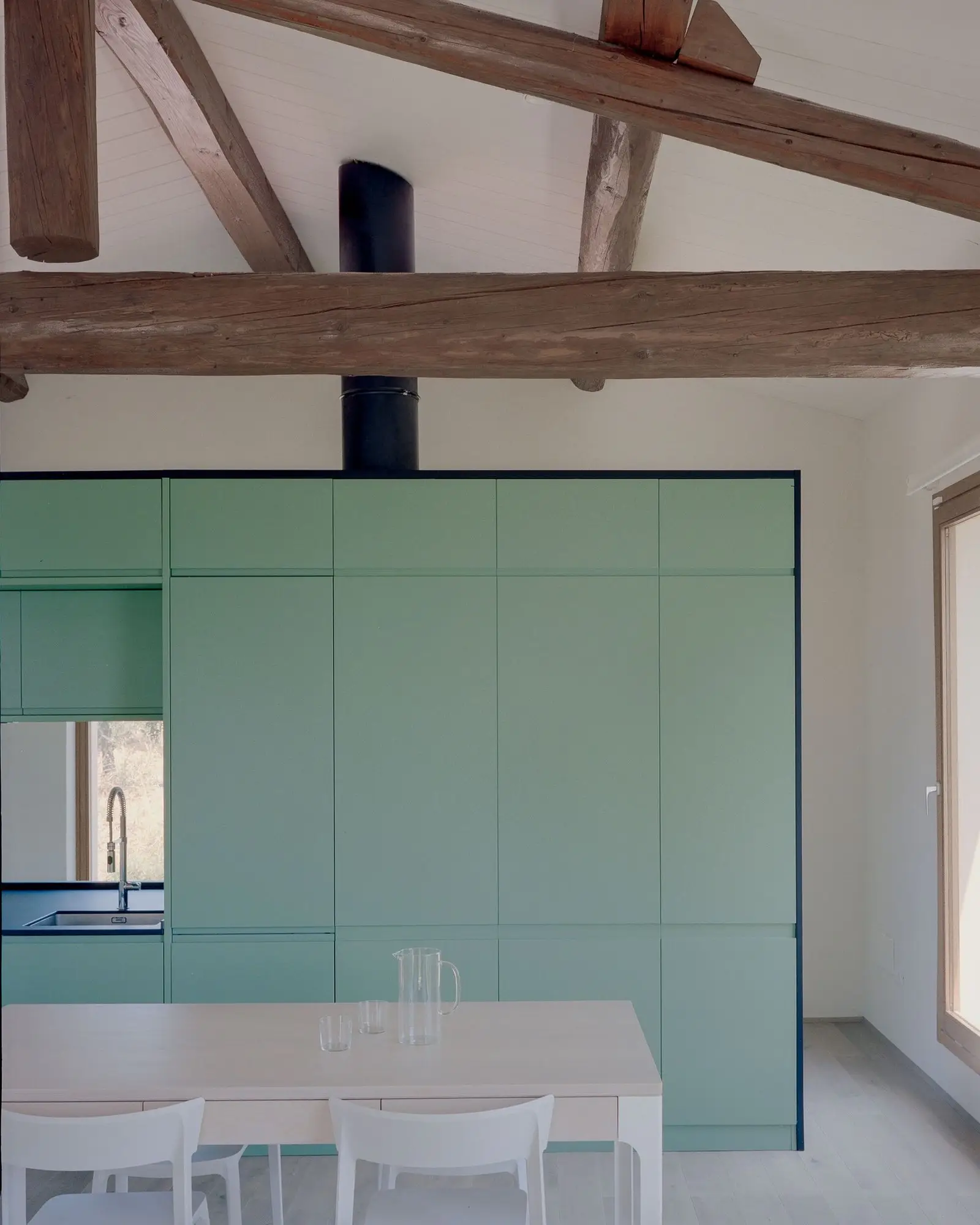 Cocina verde multifuncional y comedor bajo las cerchas originales de madera